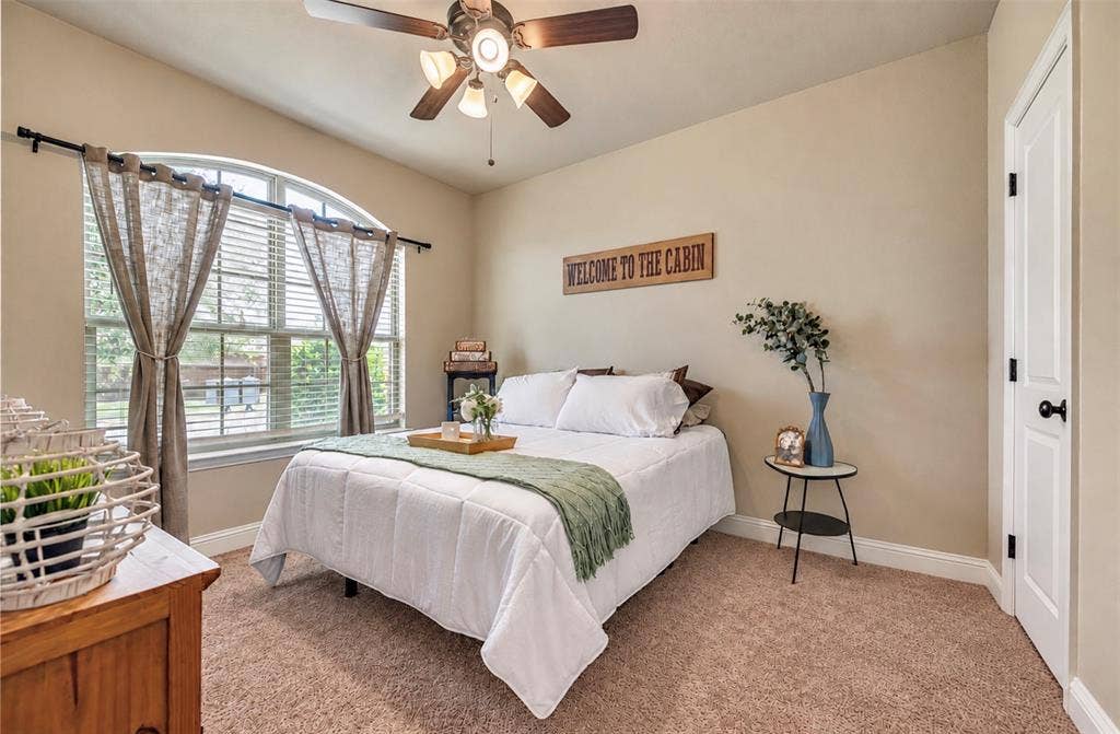 Arched window with natural light, neutral wall palette, plush carpeting, and ceiling fan with integrated lighting