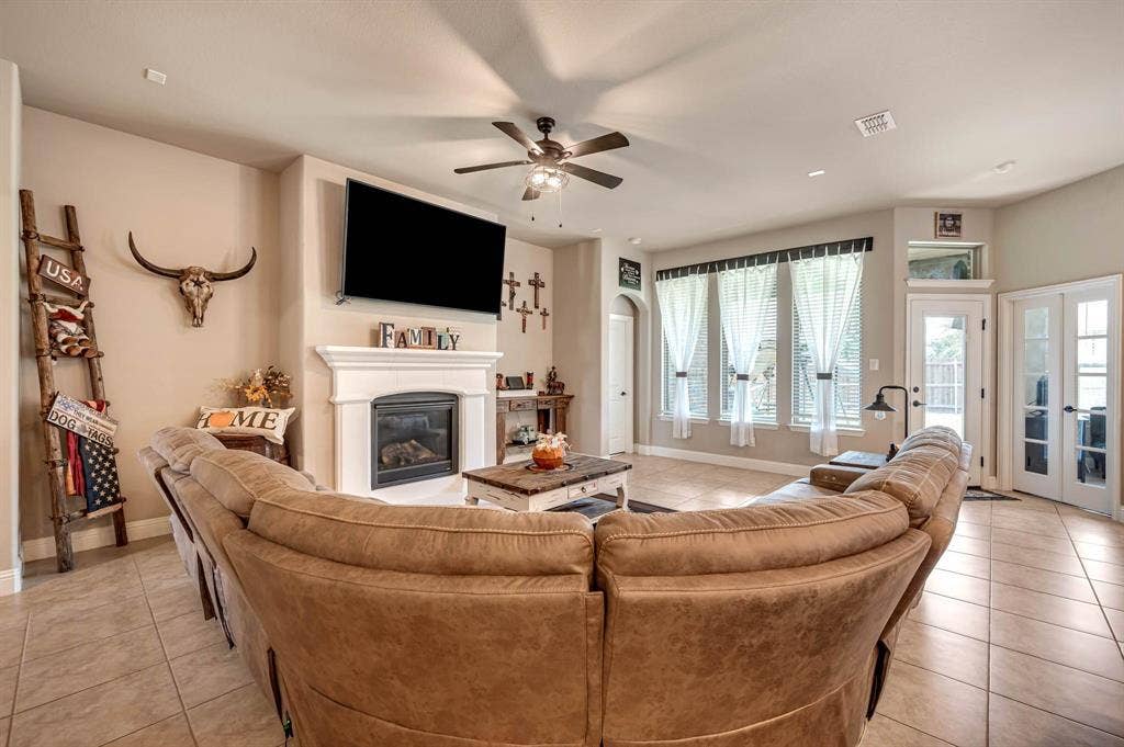Living area featuring tile flooring, a fireplace with a decorative mantel, ceiling fan, expansive windows, and a glass-paneled exterior door
