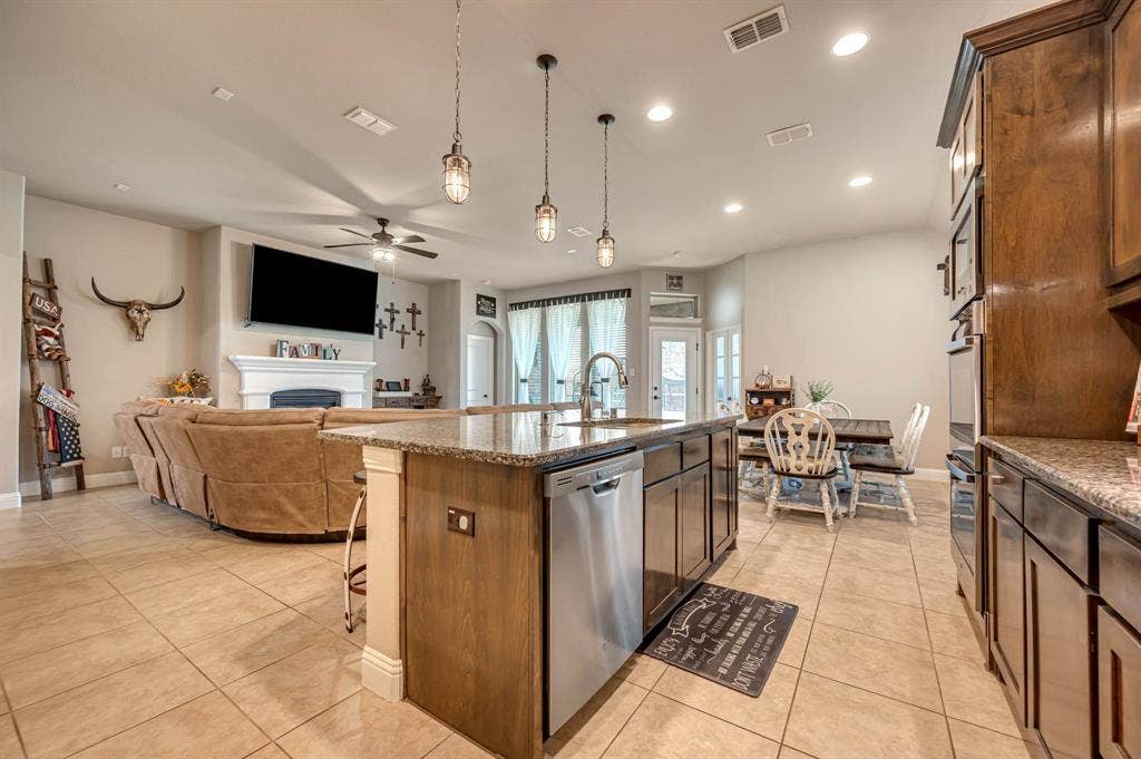 Kitchen featuring stone-surface countertops, wood-finish cabinetry, stainless steel dishwasher, recessed lighting, and trio of pendant lights