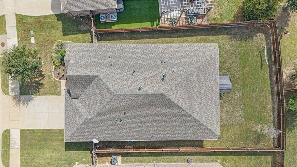 Aerial perspective featuring a multi-faceted asphalt shingle roof, a fenced backyard, and concrete hardscaping
