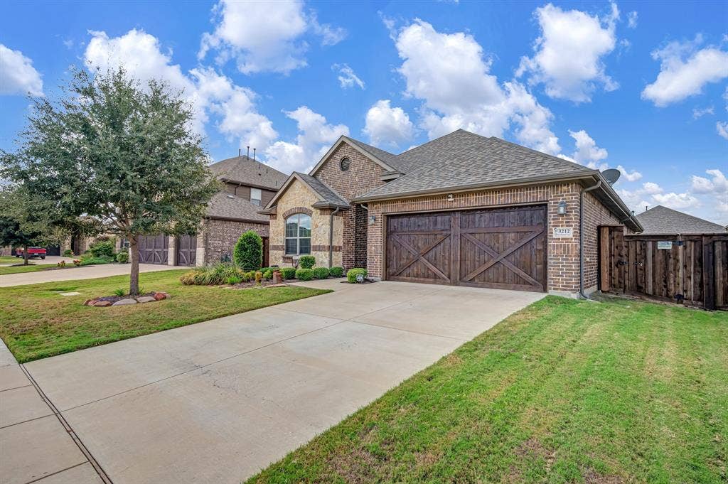 Brick and stone veneer exterior featuring a dual-bay garage with carriage-style wood-finish doors, a concrete driveway, and professional landscaping