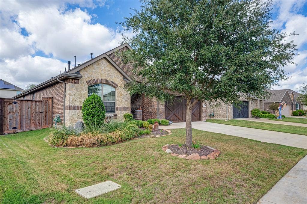 Exterior featuring a brick and stone facade, arched window detailing, wood-finish garage doors with cross-buck accents, and a concrete driveway