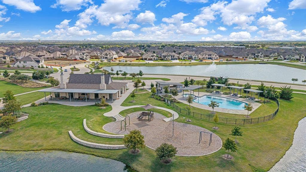 Community recreational complex featuring a swimming pool with pergola shade structures, a fenced playground area, stone retaining walls, and a multi-purpose pavilion situated on a waterfront lot