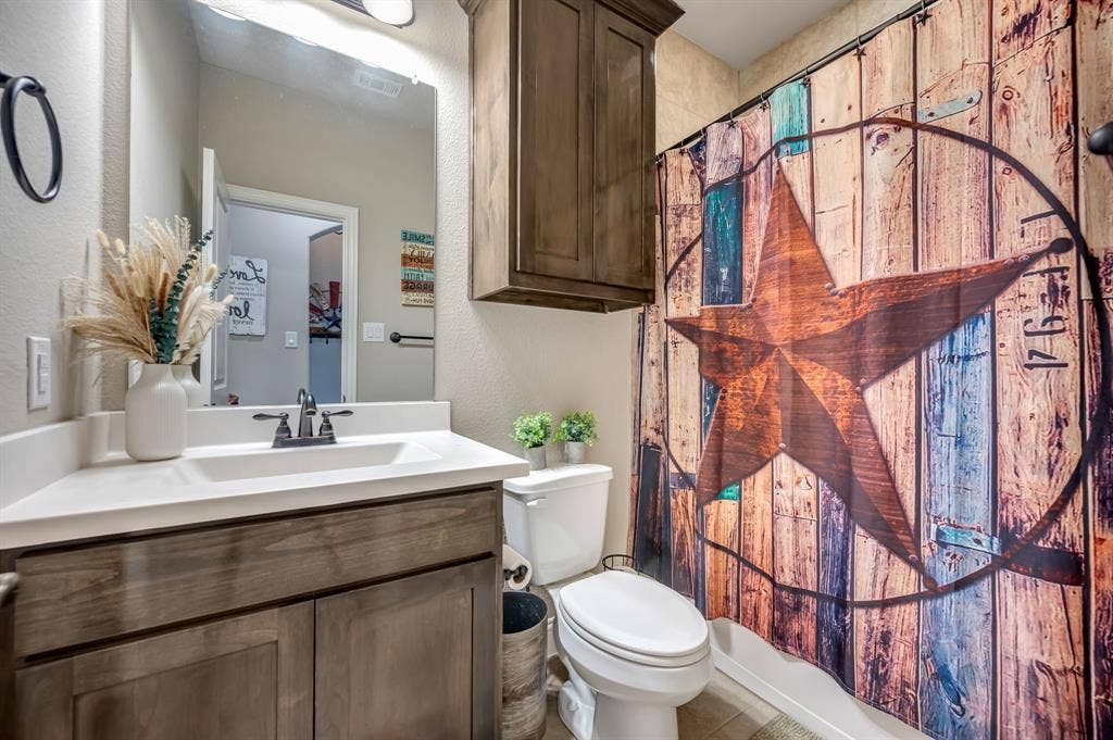 Bathroom featuring a wood-finish vanity with a rectangular sink, matte black faucet, wall-mounted cabinet, and tile flooring