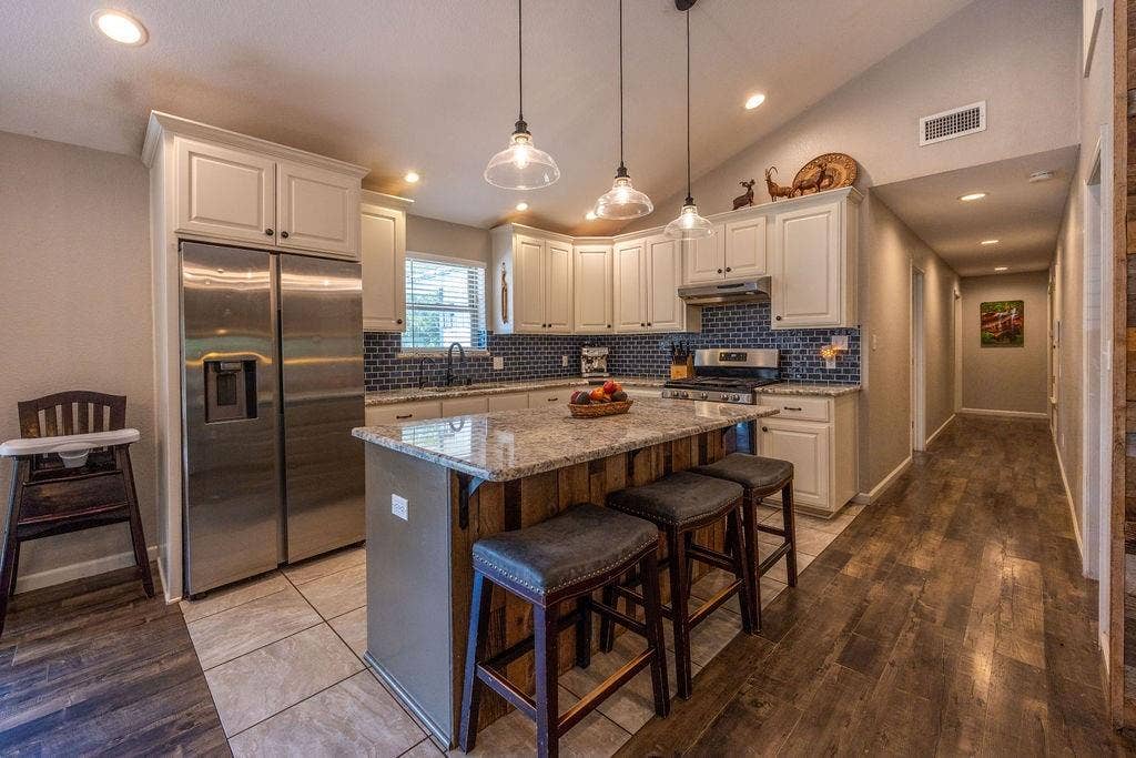 384 Fort Graham Road, Waco, TX 76705 Kitchen featuring white cabinetry, stainless steel appliances, a tile backsplash, and an island with a light-colored countertop