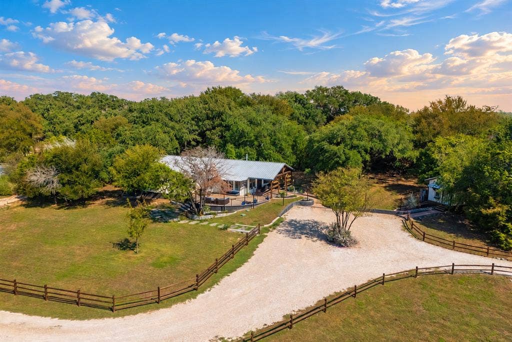 384 Fort Graham Road, Waco, TX 76705 Expansive property featuring a gravel driveway, wood fencing, a single-story residence with a metal roof, and abundant mature trees