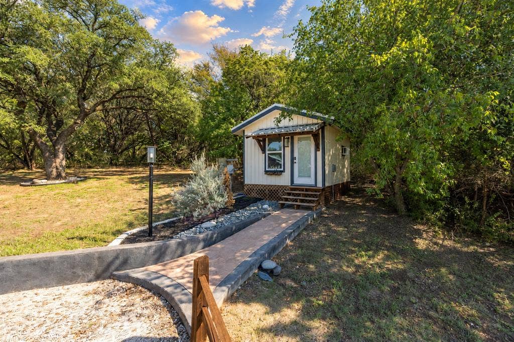 384 Fort Graham Road, Waco, TX 76705 Compact dwelling with a white facade, covered entry, and multi-level wood steps
