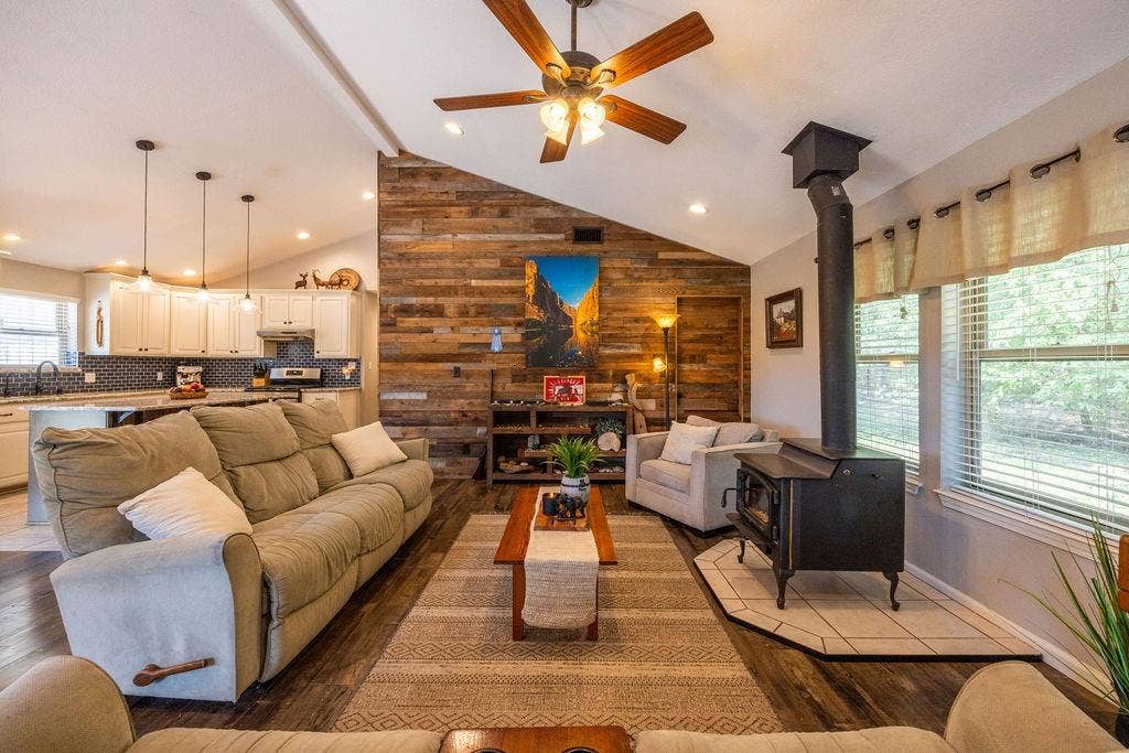 384 Fort Graham Road, Waco, TX 76705 Vaulted ceiling with a ceiling fan, wood-finish flooring, wood-paneled accent wall, and a black wood-burning stove with a tile hearth
