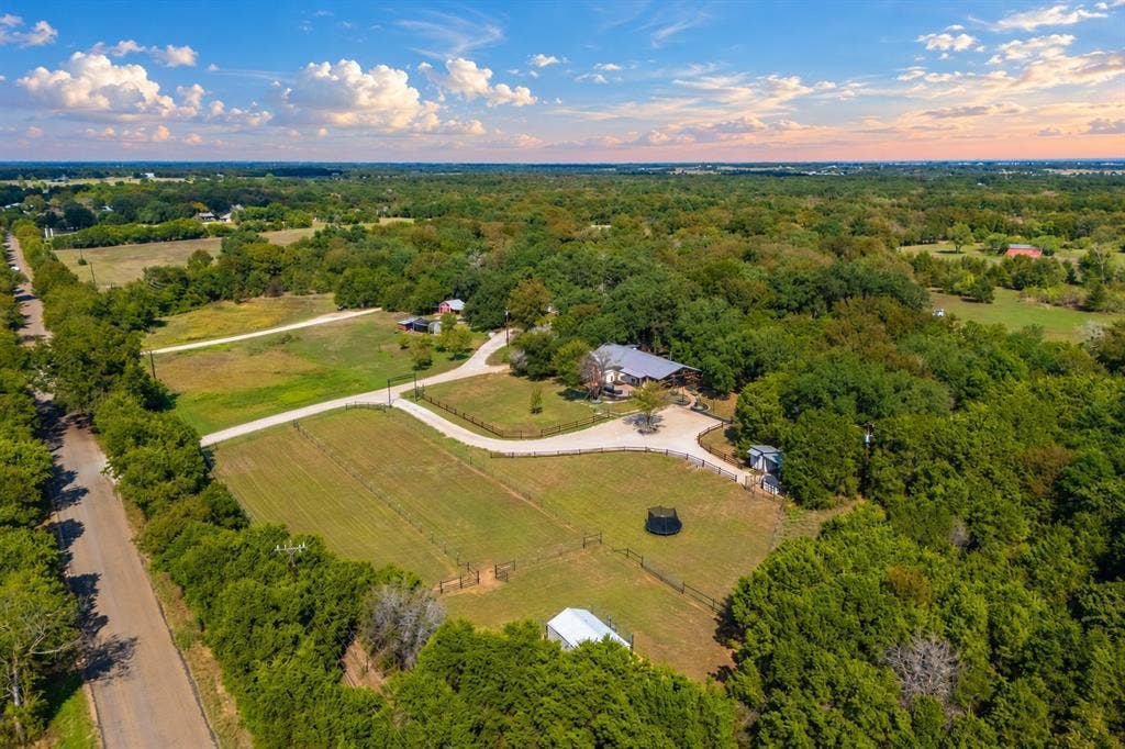 384 Fort Graham Road, Waco, TX 76705 Property featuring extensive tree coverage, open fields, a main residence with an attached garage, and a long gravel driveway