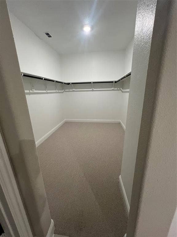 Spacious walk-in closet featuring light beige carpet, white walls, built-in shelving, and recessed lighting