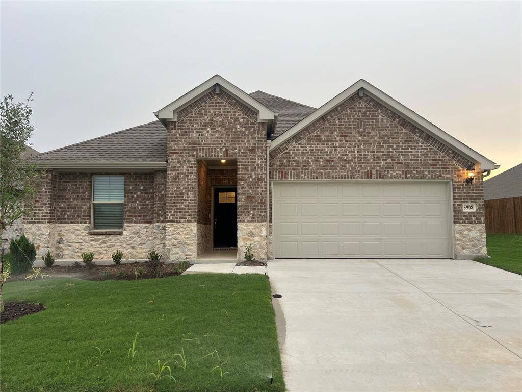 Brick and stone exterior with an attached garage, covered entry, and concrete driveway