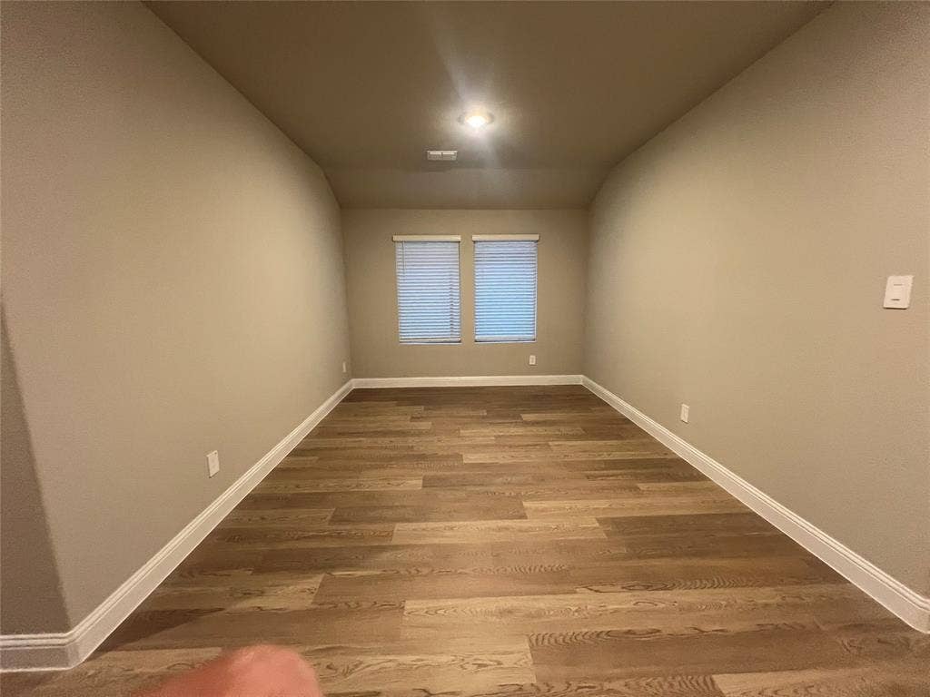 Recessed lighting illuminating wood-finish flooring, two windows with blinds, and neutral wall tones