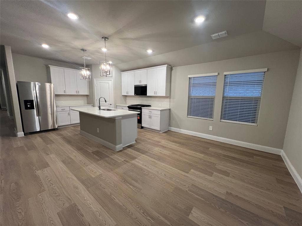 Open-concept kitchen and living area featuring wood-finish flooring, white cabinetry, a kitchen island with sink, and recessed lighting