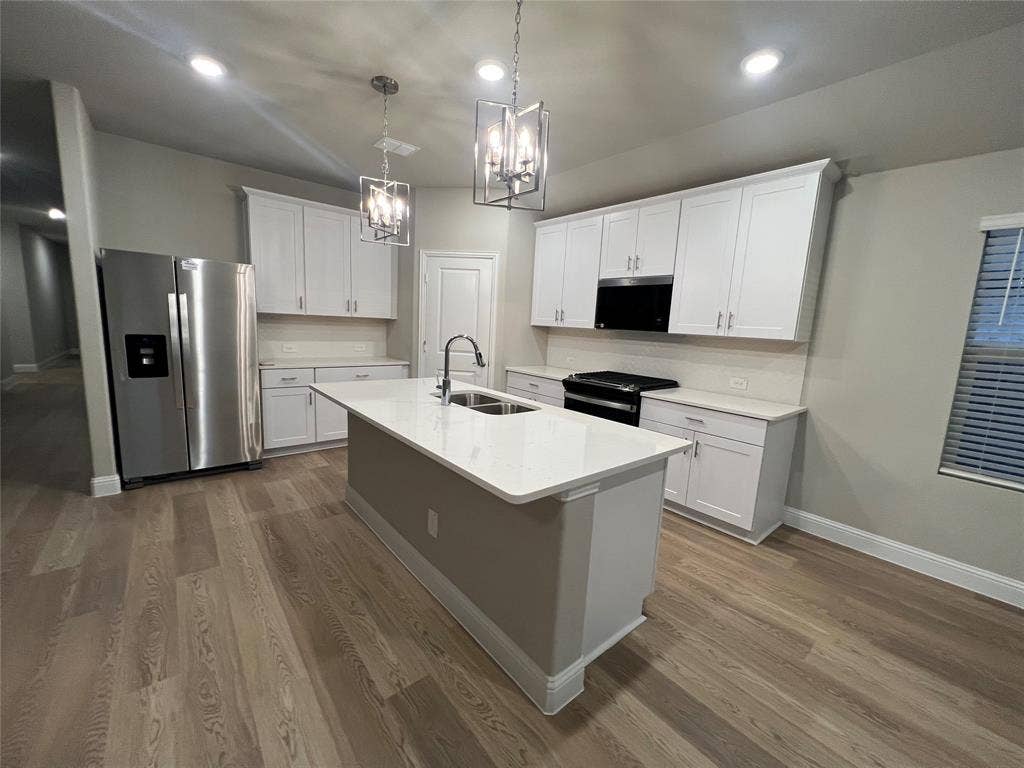 Kitchen featuring white cabinetry, wood-finish flooring, a central island with an undermount sink, pendant lighting, and stainless steel appliances