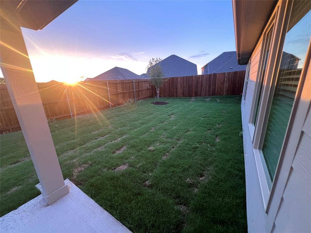 Expansive backyard with a manicured lawn, full privacy fencing, and a covered patio area