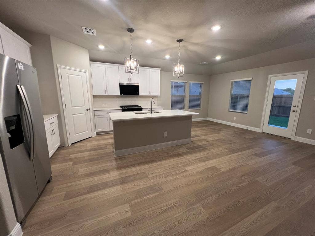 Open-concept kitchen and living area featuring wood-finish flooring, white cabinetry, a kitchen island with sink, stainless steel appliances, and recessed lighting