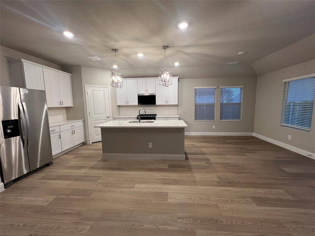 Spacious open-concept living area with wood-finish flooring, recessed lighting, and a kitchen island with pendant lighting