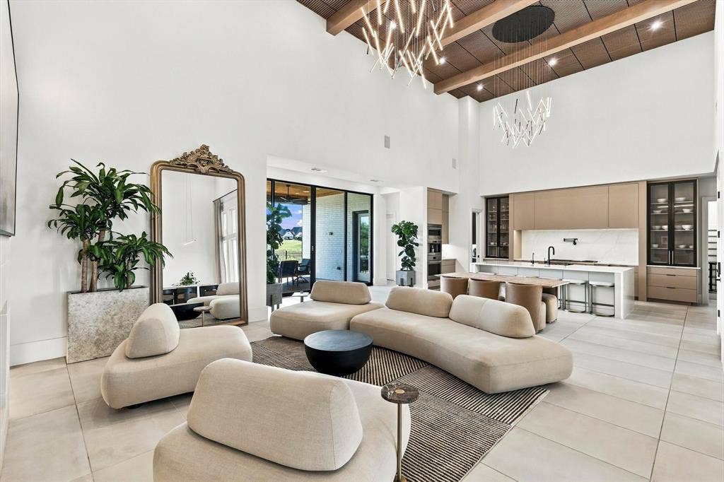4301 Corabelle Lane, Prosper, TX 75078 Two-story ceiling with exposed wood beams, modern overhead lighting, recessed lighting, expansive glass sliding doors, and a kitchen featuring a large island with seating