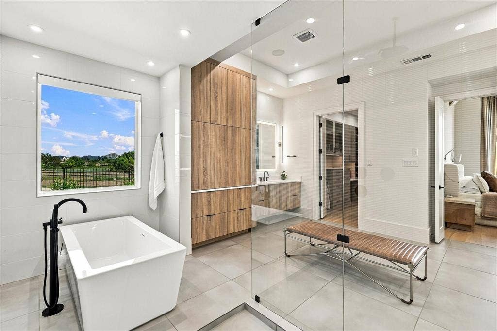 4301 Corabelle Lane, Prosper, TX 75078 Freestanding soaking tub with a matte black floor-mounted faucet, a wood-finish vanity with an undermount sink, and a glass-enclosed shower
