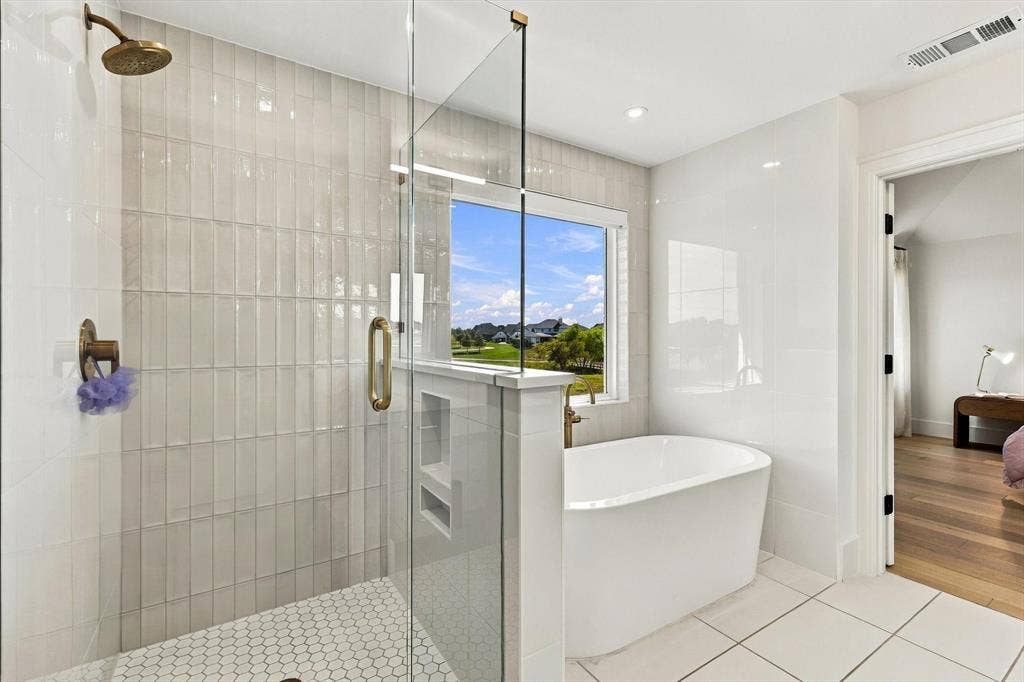 4301 Corabelle Lane, Prosper, TX 75078 Frameless glass shower with brass fixtures, a freestanding soaking tub, and a window providing natural light