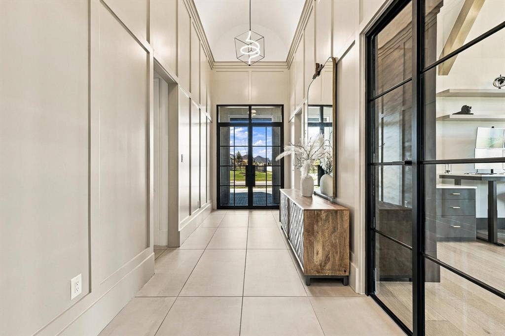 4301 Corabelle Lane, Prosper, TX 75078 Board and batten wall detailing, arched ceiling, contemporary chandelier, black-framed glass entry door, and large format tile flooring