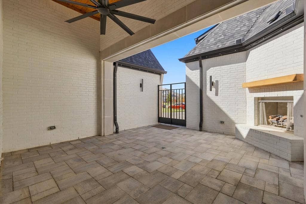 4301 Corabelle Lane, Prosper, TX 75078 Covered outdoor patio featuring a ceiling fan, brick fireplace with wood mantle, paver flooring, and a metal gate