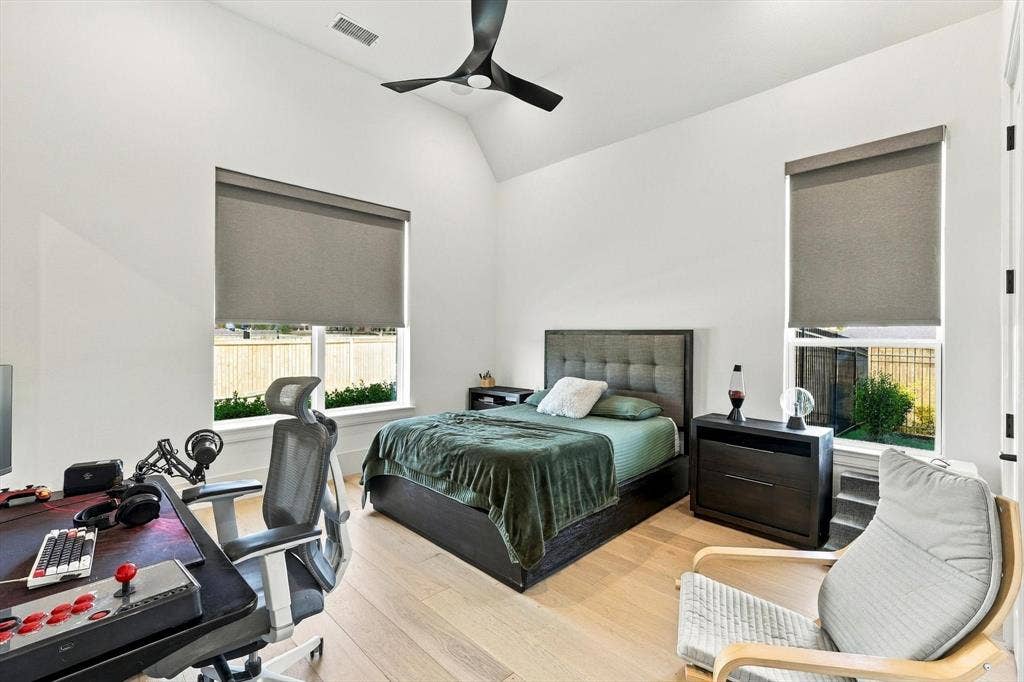 4301 Corabelle Lane, Prosper, TX 75078 Vaulted ceiling with a contemporary ceiling fan, light wood-finish flooring, two large windows with roller shades, and a built-in bed frame with a tufted headboard