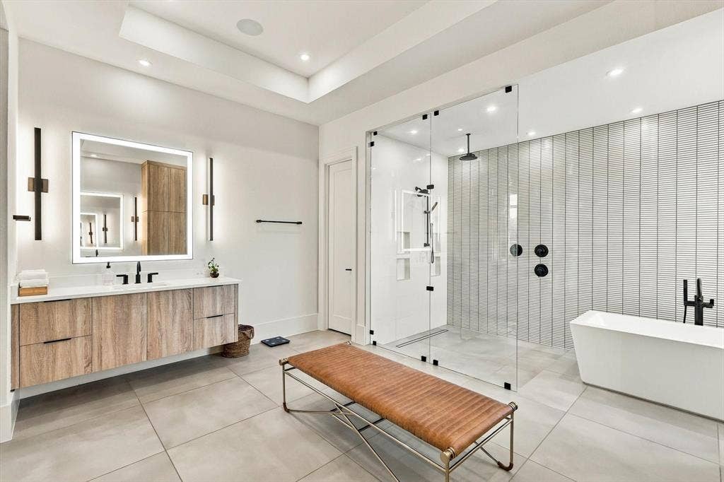 4301 Corabelle Lane, Prosper, TX 75078 Floating wood-finish vanity with an illuminated mirror, glass-enclosed shower, freestanding bathtub, and large format floor tiling
