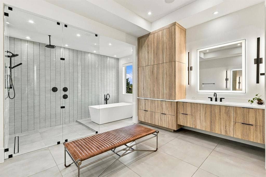 4301 Corabelle Lane, Prosper, TX 75078 Spacious bathroom featuring a glass-enclosed shower with multiple showerheads, a freestanding soaking tub, wood-finish cabinetry, a large vanity with an integrated mirror, and light-toned tile flooring