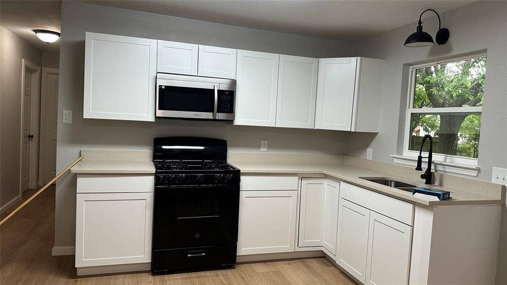 White shaker cabinetry, light-toned countertops, stainless steel microwave, black gas range, and wood-finish flooring