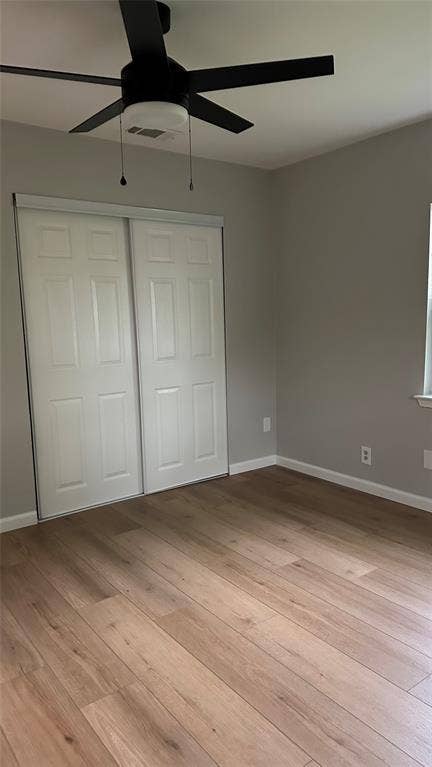 Wood-finish flooring, sliding closet doors, ceiling fan with integrated lighting, and neutral wall paint