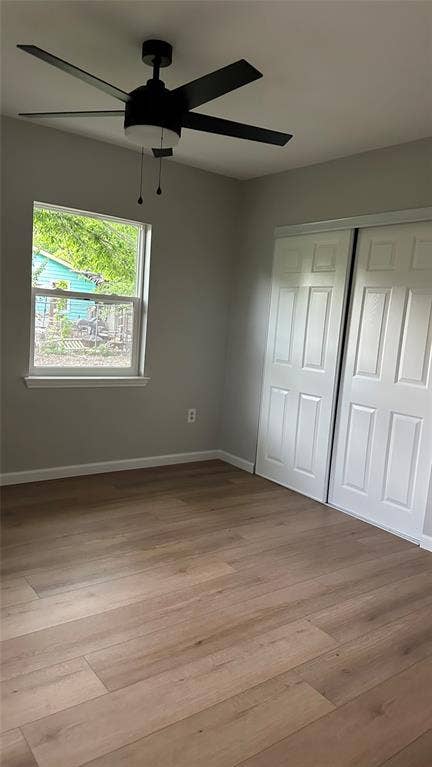 Wood-finish flooring, white bi-fold closet doors, ceiling fan with integrated lighting, and a single window