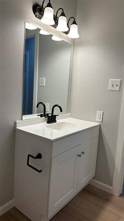 White vanity with shaker-style cabinet doors, integrated sink, and a black-finish faucet