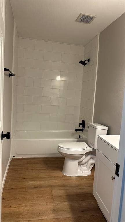 Wood-finish flooring, white subway tile shower surround, white bathtub, white vanity with shaker-style door, and matte black fixtures