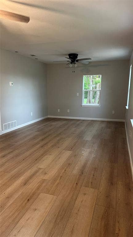 Spacious room featuring wood-finish flooring, neutral wall tones, a ceiling fan, and a double-hung window