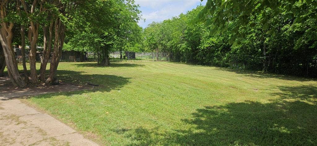 Expansive grassy lot featuring mature trees and a paved path