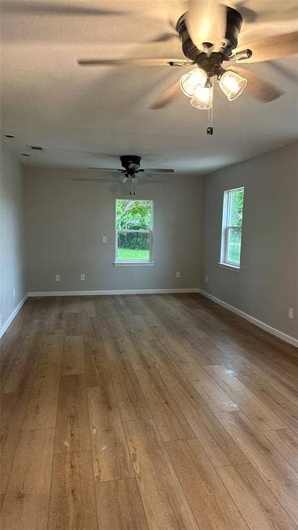 Wood-finish flooring, neutral wall tones, two ceiling fans with integrated lighting, and multiple windows