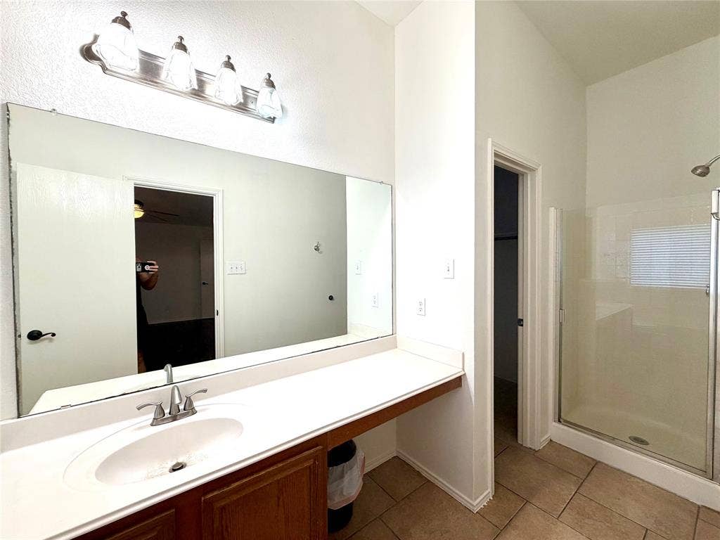 9016 Warren Drive, McKinney, TX 75071 Bathroom featuring a single-sink vanity with a solid-surface countertop, a full-width wall mirror, a four-light fixture, and a glass-enclosed shower stall with tile flooring