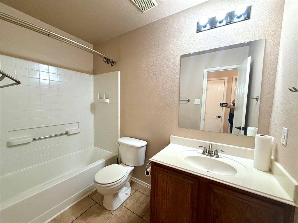 9016 Warren Drive, McKinney, TX 75071 Bathroom featuring wood-finish vanity cabinetry, integrated countertop with oval basin, wall-mounted mirror, three-light fixture, and tub-shower combination with tile-finish surround