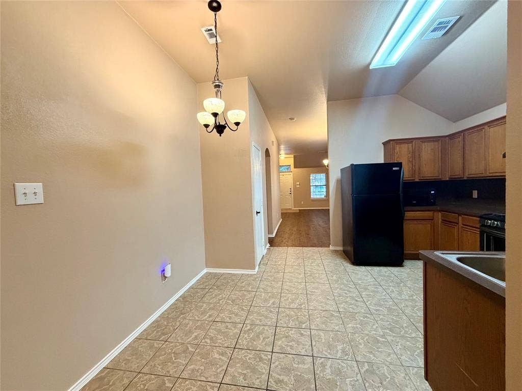 9016 Warren Drive, McKinney, TX 75071 Ceramic tile flooring, stained wood cabinetry, vaulted ceiling with integrated lighting, and three-bulb hanging chandelier