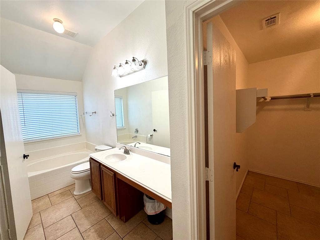 9016 Warren Drive, McKinney, TX 75071 Bathroom featuring tile flooring, a soaking tub with a tiled surround, a vanity with a solid-surface countertop, and an attached walk-in closet with built-in shelving
