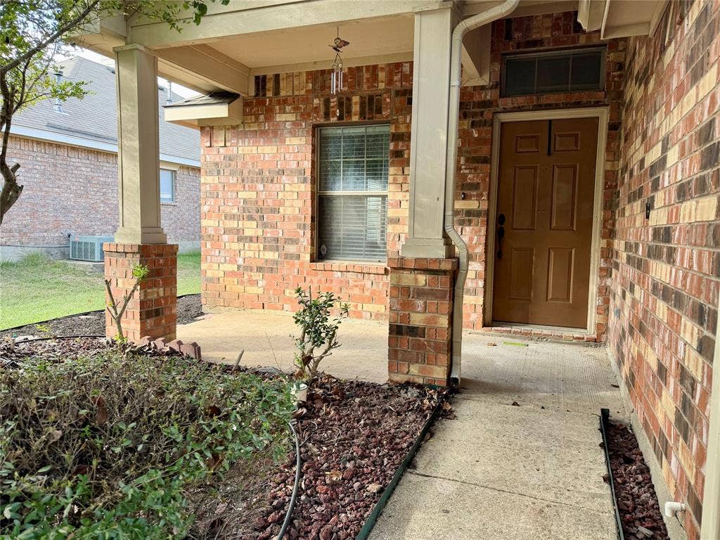 9016 Warren Drive, McKinney, TX 75071 This photograph features the charming brick exterior of the property, highlighting a welcoming covered front porch, and a sturdy solid-panel front door enhanced by an attractive integrated transom window that allows for natural light.