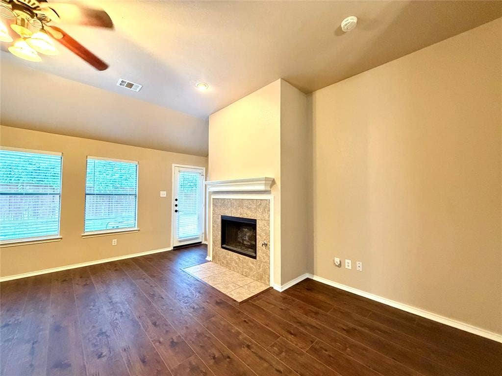 9016 Warren Drive, McKinney, TX 75071 Vaulted ceiling with a central paddle fan, wood-finish flooring, and a fireplace featuring a tile surround and a crown-molding mantle