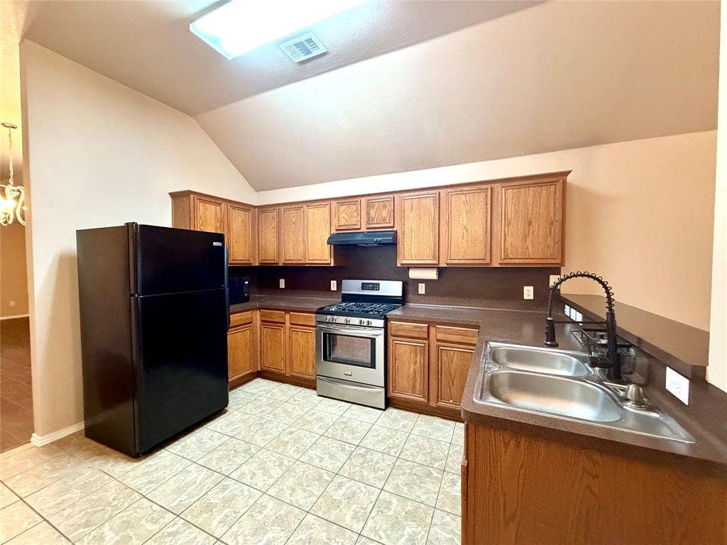 9016 Warren Drive, McKinney, TX 75071 Kitchen featuring wood cabinetry, vaulted ceiling, double-basin stainless steel sink with matte black faucet, and stainless steel gas range