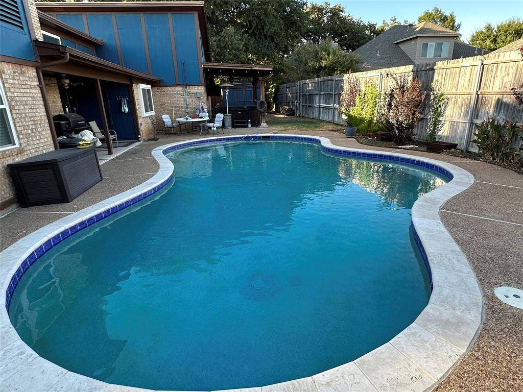 Freeform swimming pool with blue tile accents, concrete decking, and an adjacent covered patio area