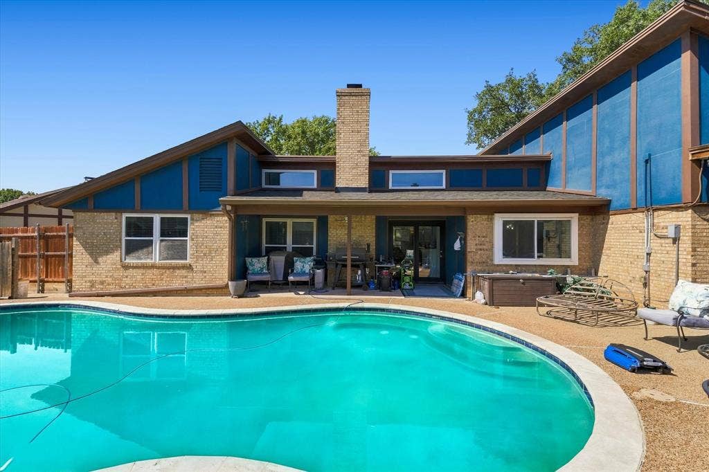 Exterior featuring a freeform swimming pool, brick facade, covered patio, and large windows