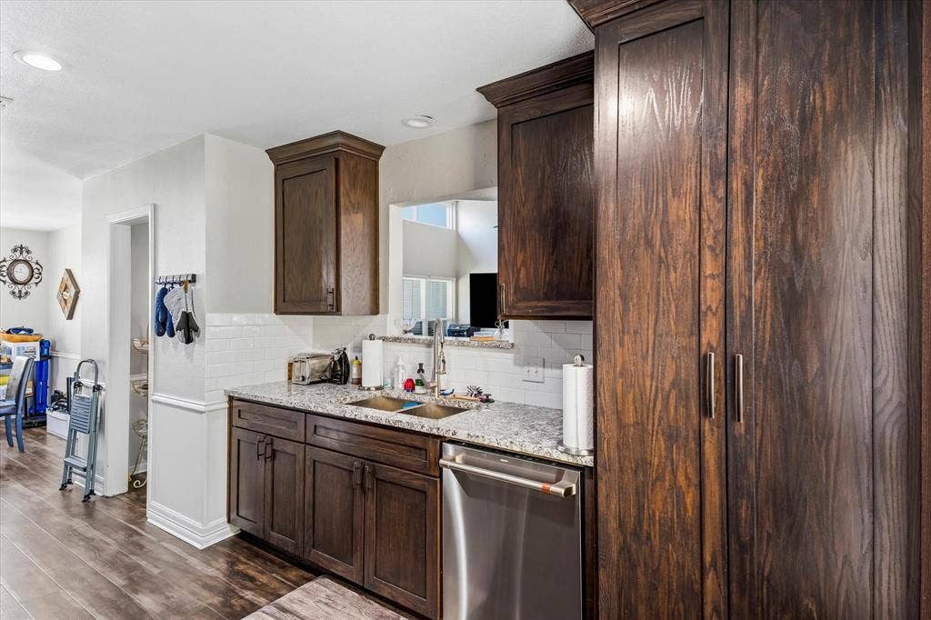 Kitchen featuring wood-finish flooring, dark wood cabinetry, a white subway tile backsplash, and a double basin sink with a chrome faucet