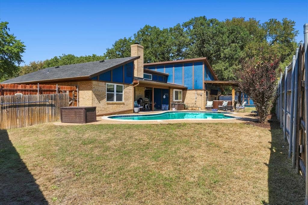 Brick exterior with a peaked roofline, featuring an in-ground swimming pool, a covered patio, and a privacy fence
