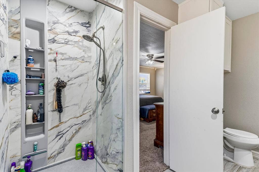 Walk-in shower with glass enclosure, marble-look wall tiling, and built-in shelving