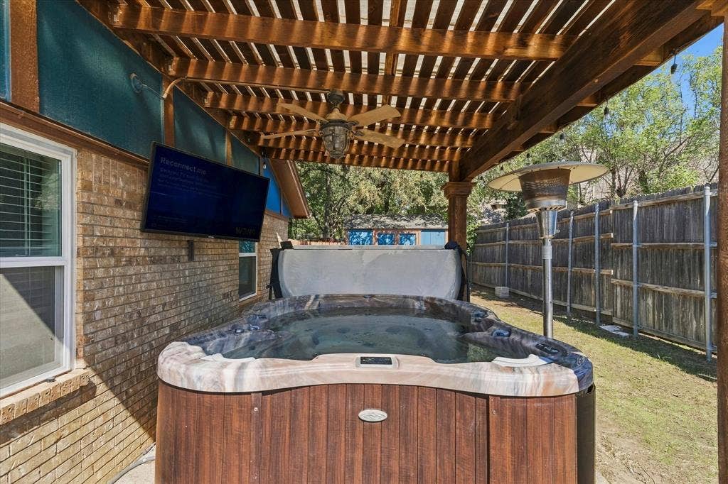 Wood pergola with a ceiling fan, brick exterior, and a built-in hot tub